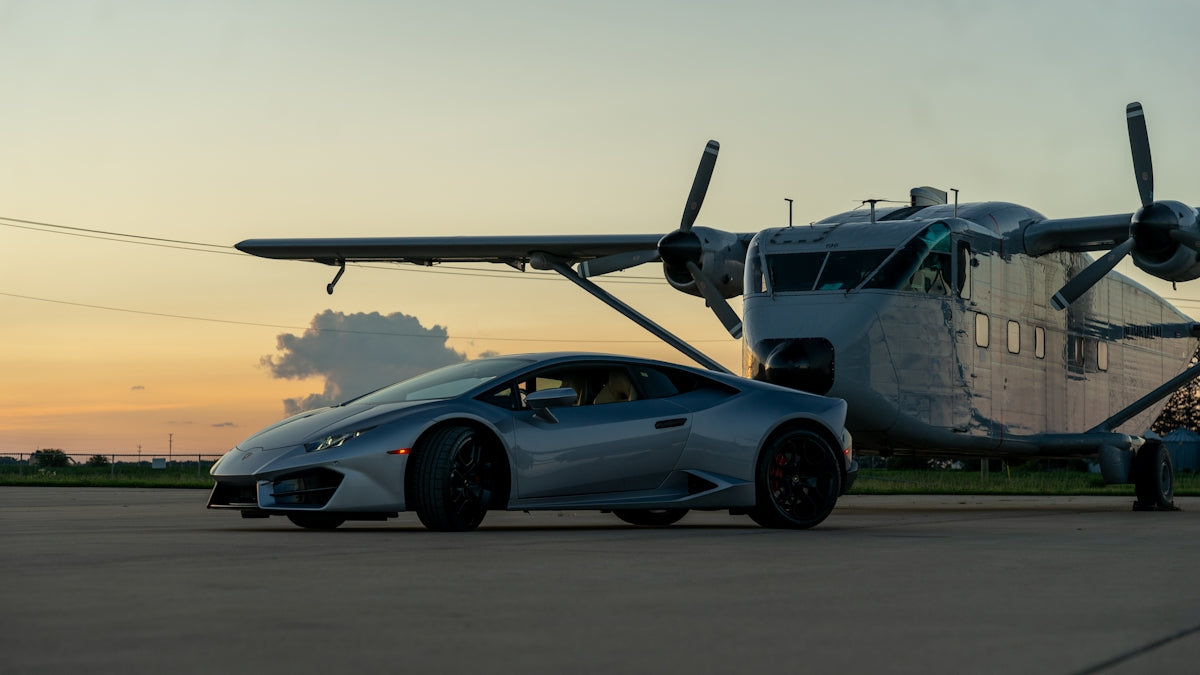 A silver sports car parked next to an airplane
